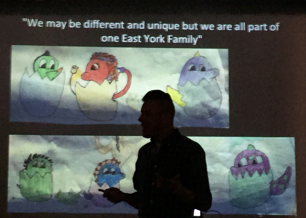 Mosaic artist Justin Ayala is silhouetted against a slide showing the plans for a mural at East York Elementary School.